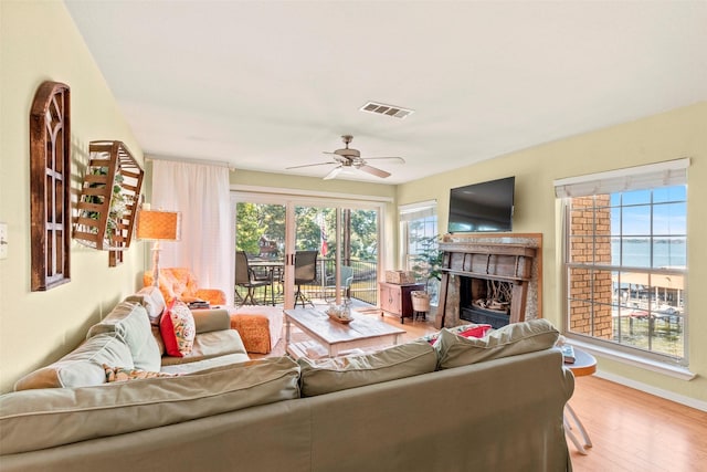 living room with a fireplace, a ceiling fan, baseboards, wood finished floors, and visible vents