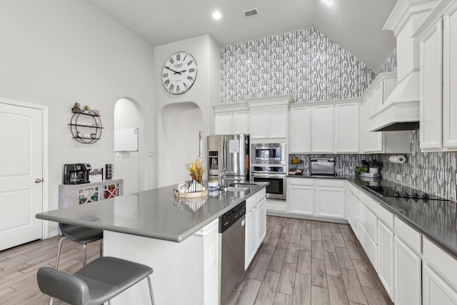 kitchen with custom range hood, visible vents, stainless steel appliances, and wood finish floors