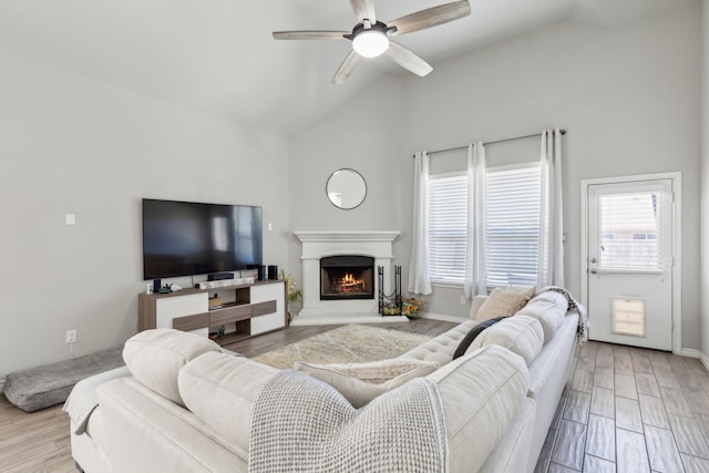 living room featuring lofted ceiling, a ceiling fan, wood finished floors, a warm lit fireplace, and baseboards