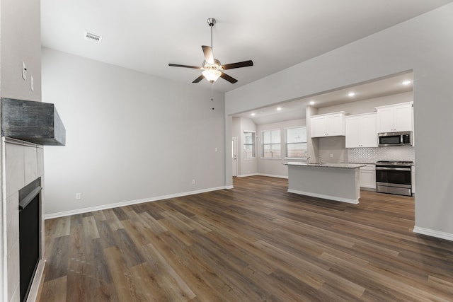 unfurnished living room featuring a tile fireplace, visible vents, baseboards, a ceiling fan, and dark wood-style floors