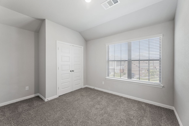 unfurnished bedroom featuring lofted ceiling, visible vents, dark carpet, and baseboards