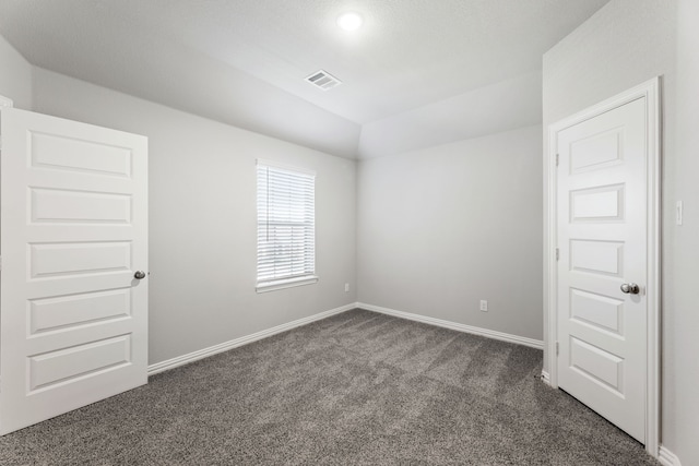 unfurnished room featuring lofted ceiling, baseboards, visible vents, and dark carpet