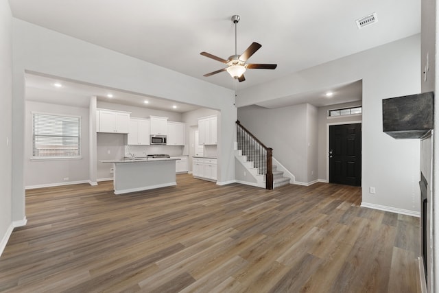 unfurnished living room with wood finished floors, visible vents, ceiling fan, and stairs