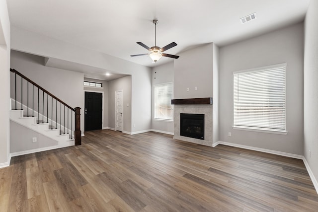 unfurnished living room with visible vents, stairway, a tiled fireplace, and wood finished floors