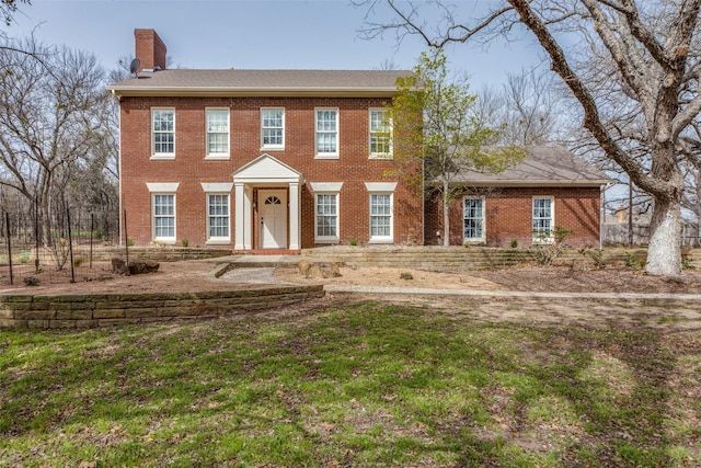 colonial house featuring a front yard, brick siding, and a chimney