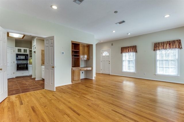 unfurnished living room featuring built in desk, recessed lighting, light wood-type flooring, and visible vents