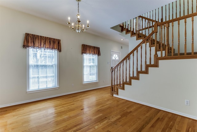 entrance foyer with a chandelier, stairway, baseboards, and wood finished floors