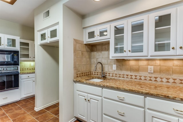 kitchen with black appliances, light stone countertops, visible vents, and a sink