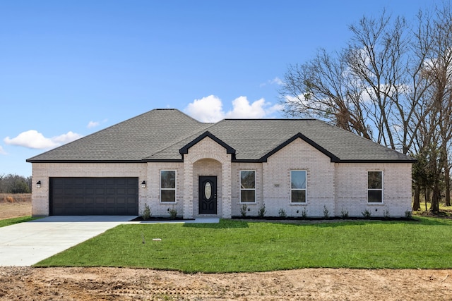 french country style house featuring brick siding, a shingled roof, an attached garage, a front yard, and driveway