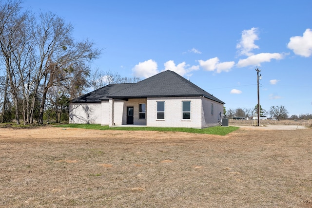 back of property with brick siding, a lawn, and central AC