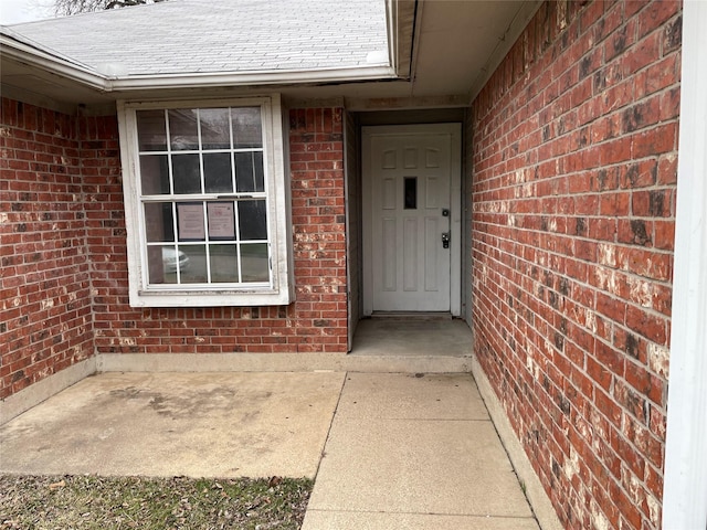 property entrance featuring brick siding and roof with shingles