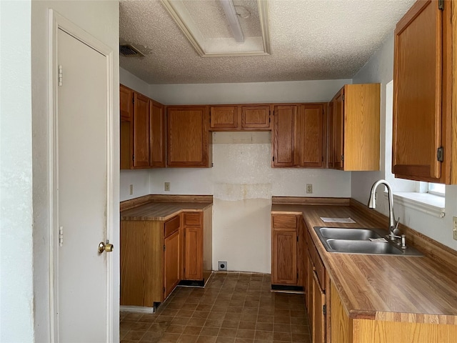 kitchen featuring visible vents, brown cabinets, a sink, and a textured ceiling