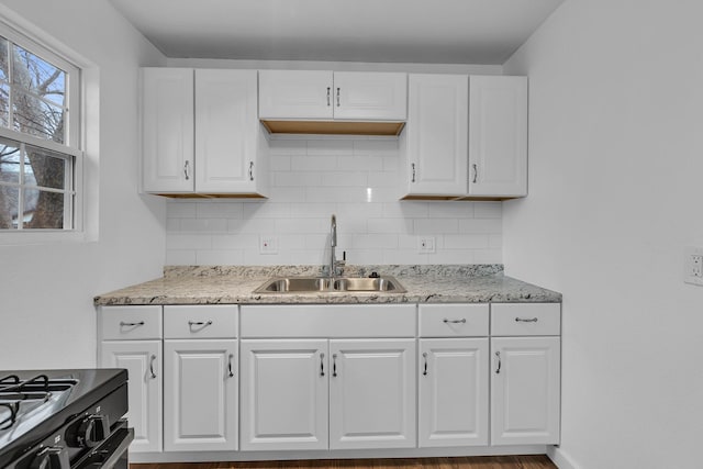 kitchen with white cabinetry, backsplash, a sink, and gas stove