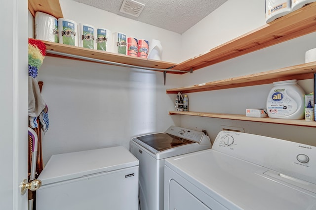 clothes washing area featuring a textured ceiling, laundry area, washing machine and clothes dryer, and visible vents