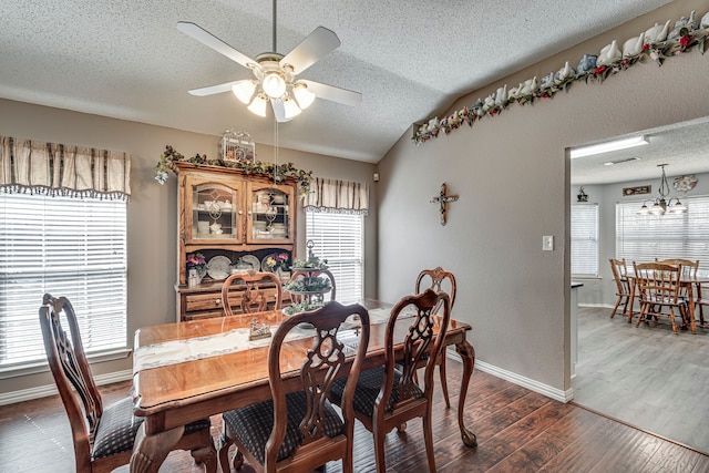 dining space featuring dark wood-style floors, vaulted ceiling, a textured ceiling, baseboards, and ceiling fan with notable chandelier