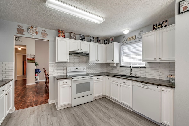 kitchen featuring white appliances, light wood finished floors, dark countertops, under cabinet range hood, and a sink