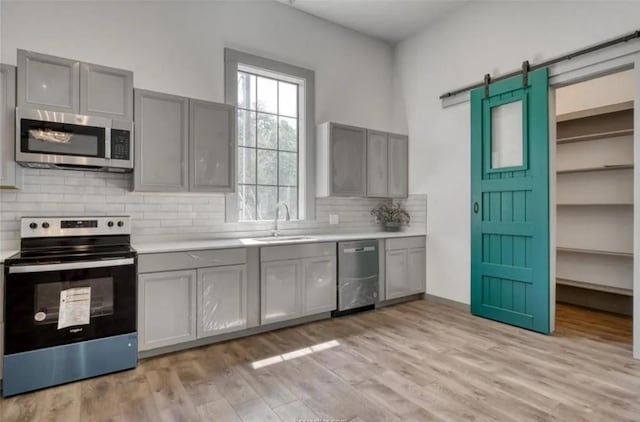 kitchen featuring gray cabinets, light countertops, a barn door, appliances with stainless steel finishes, and a sink