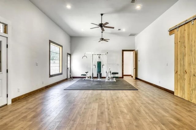 workout area with a barn door, a high ceiling, wood finished floors, a ceiling fan, and baseboards