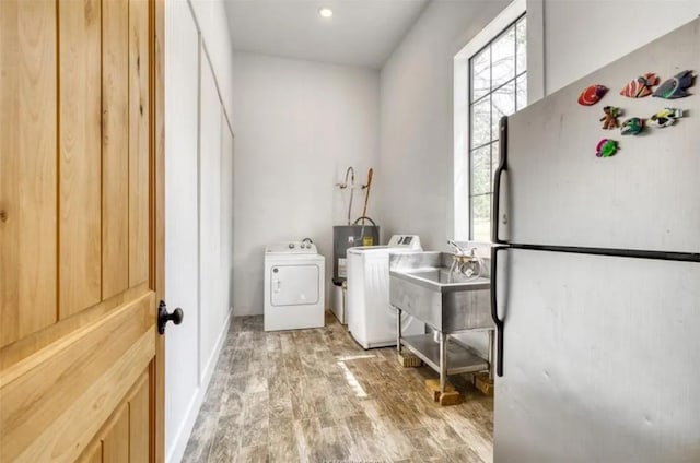 washroom with laundry area, light wood finished floors, washer and clothes dryer, and a sink