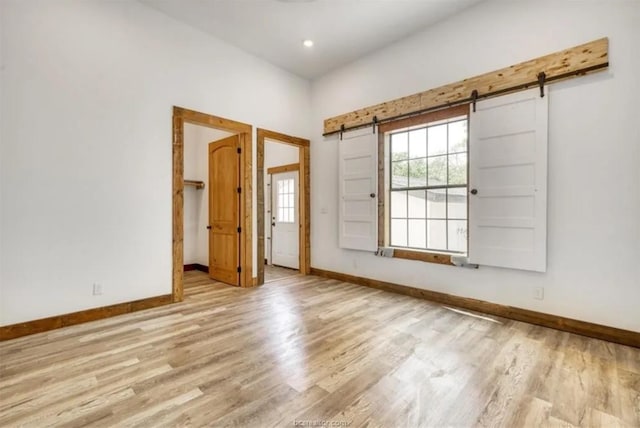 unfurnished room featuring a barn door, recessed lighting, wood finished floors, and baseboards