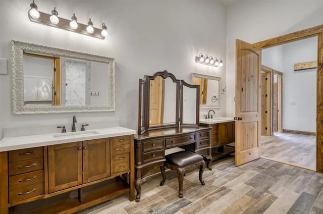 full bath featuring wood finished floors, two vanities, a sink, and baseboards