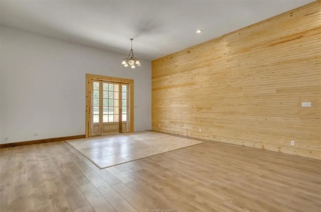 empty room with an inviting chandelier, light wood-style flooring, wooden walls, and baseboards