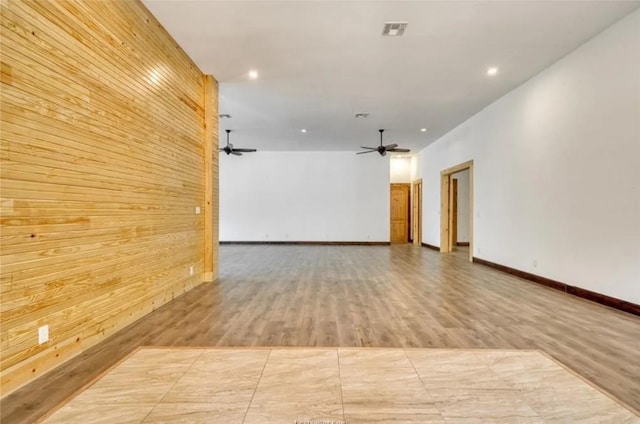 spare room with a ceiling fan, wood finished floors, visible vents, and wooden walls