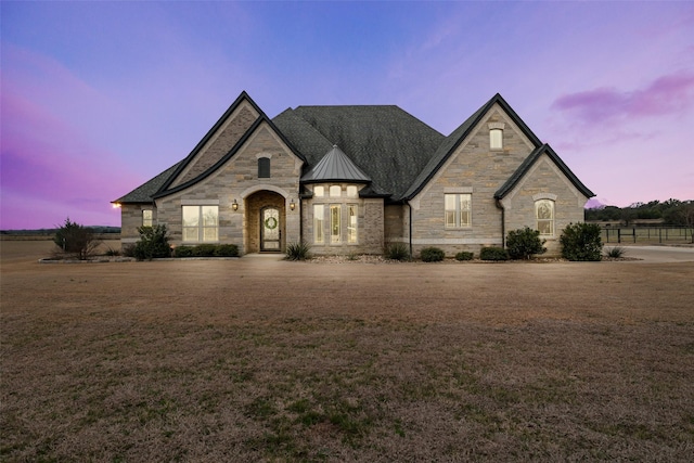 french country inspired facade featuring a standing seam roof, metal roof, a lawn, and stone siding