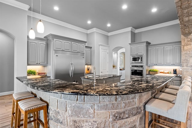 kitchen with a breakfast bar, arched walkways, a large island, gray cabinetry, and built in appliances