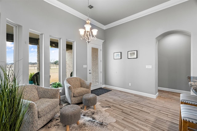 living area featuring arched walkways, a notable chandelier, baseboards, light wood-type flooring, and crown molding