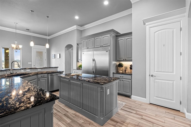 kitchen featuring arched walkways, a kitchen island, stainless steel appliances, gray cabinetry, and a sink