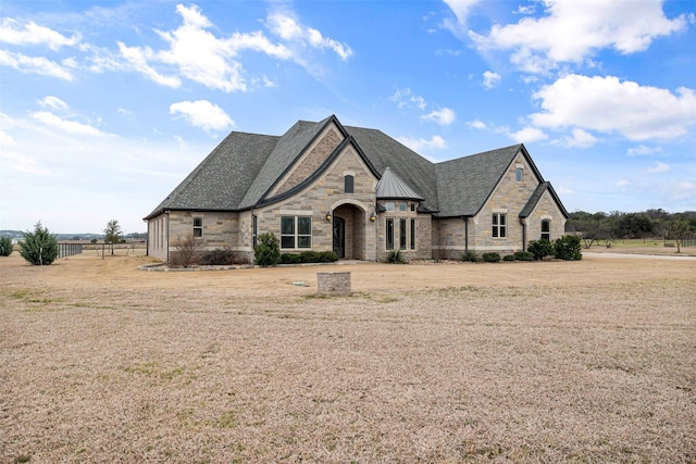 french country style house with stone siding and a front lawn