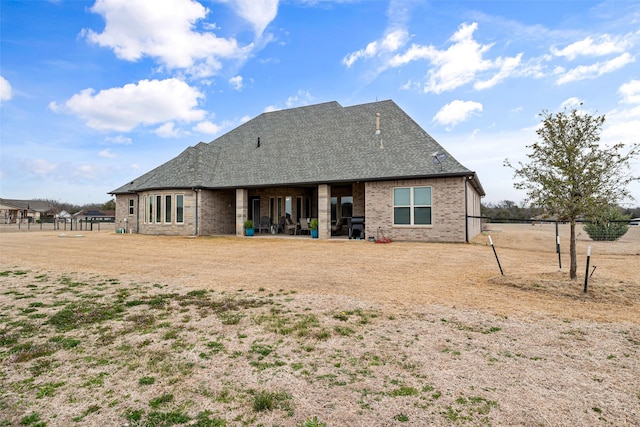 rear view of property featuring brick siding and roof with shingles