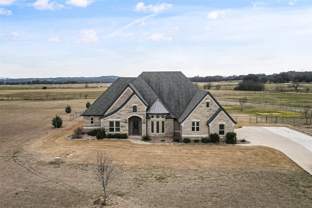 french country style house featuring a standing seam roof, fence, metal roof, stone siding, and a rural view