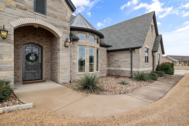 doorway to property featuring metal roof, stone siding, brick siding, and roof with shingles