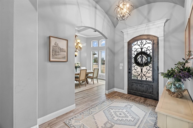 foyer entrance with light wood-type flooring, arched walkways, baseboards, and an inviting chandelier