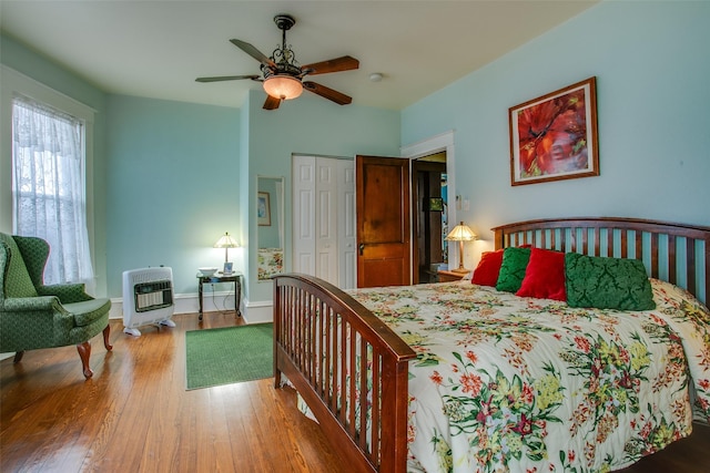 bedroom featuring baseboards, ceiling fan, wood finished floors, heating unit, and a closet