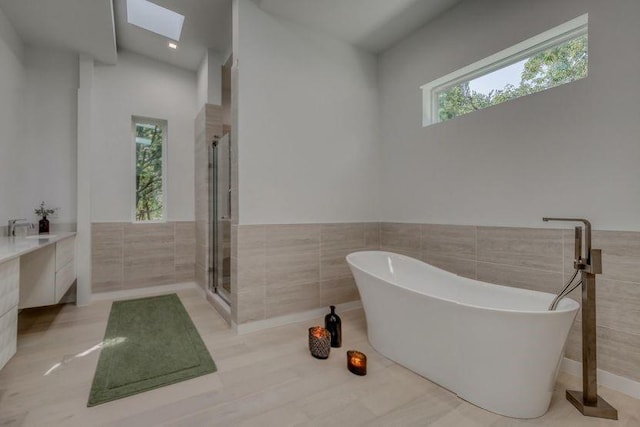 bathroom with a skylight, a wainscoted wall, tile walls, a soaking tub, and a stall shower