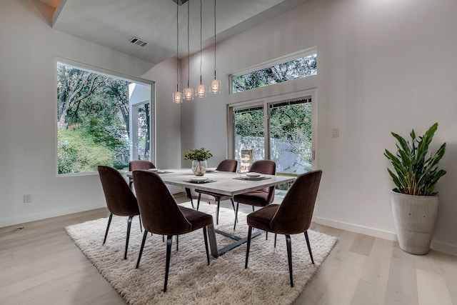 dining area with light wood-type flooring, a towering ceiling, visible vents, and baseboards