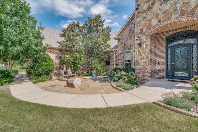 entrance to property featuring stone siding, a shingled roof, a patio, and brick siding