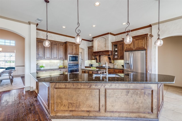 kitchen featuring stainless steel appliances, arched walkways, custom range hood, and a spacious island