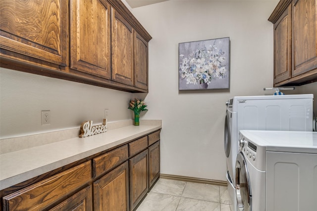 clothes washing area featuring separate washer and dryer, light tile patterned flooring, cabinet space, and baseboards