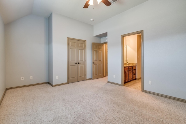 unfurnished bedroom featuring light carpet, baseboards, vaulted ceiling, a closet, and ensuite bath