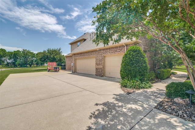 view of side of property with a garage, concrete driveway, brick siding, and roof with shingles