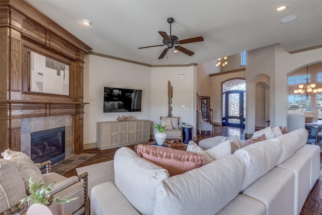 living room with arched walkways, a tiled fireplace, stairway, crown molding, and recessed lighting