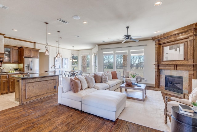 living room with plenty of natural light, visible vents, crown molding, and a tiled fireplace