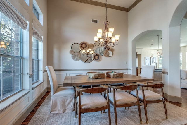 dining space featuring a chandelier, arched walkways, wood finished floors, visible vents, and ornamental molding