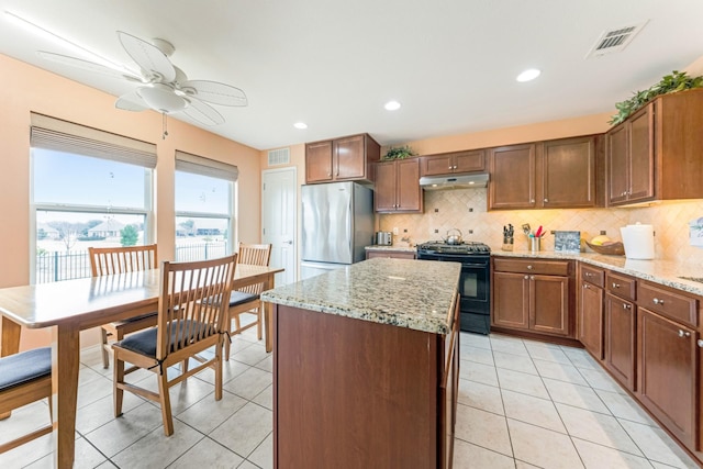 kitchen featuring visible vents, freestanding refrigerator, black range, under cabinet range hood, and backsplash