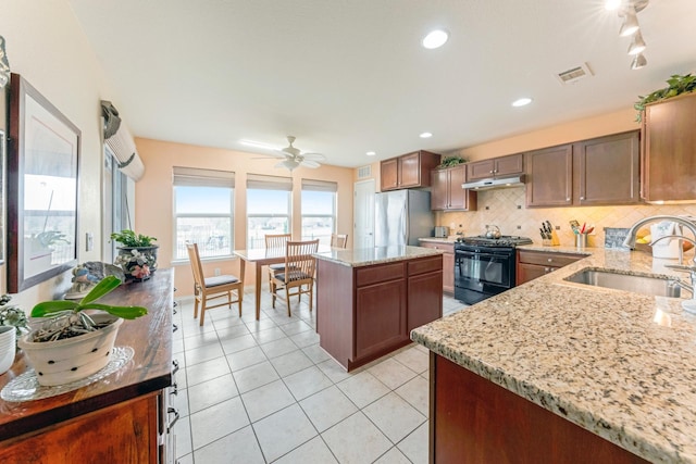 kitchen with black range, a sink, decorative backsplash, freestanding refrigerator, and a center island