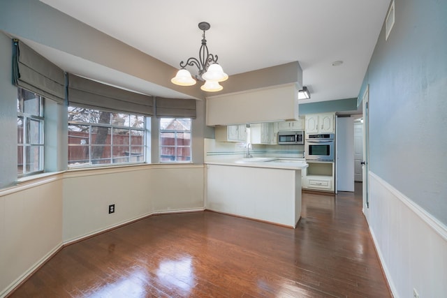 kitchen with dark wood-style flooring, a peninsula, stainless steel appliances, a sink, and a warming drawer